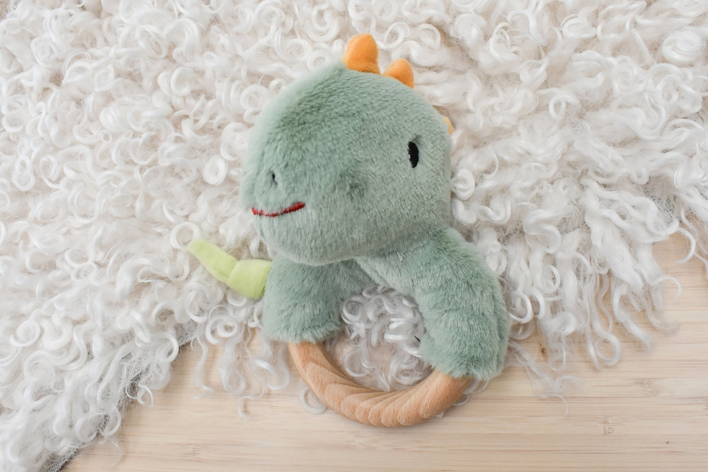 Minty dinosaur plush rattle with wooden ring for cuddly playtime and sensory stimulation.